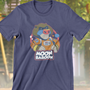 Image shows It Takes Two Moon Baboon Tee (blue) facing front. Moon Baboon has brown fur and, like an mandrill, he has blue and red markings on his face. He wears an orange jumpsuit with yellow cuffs and buttons. Moon Baboon has two patches with pictures of rockets on both his arms and one with his name on his chest. He also wears a white pack with his name printed on the back.